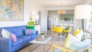 A modern living room with a blue sofa, yellow chairs, and a dining area with a round table.