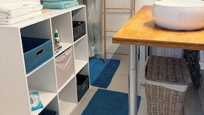 A bathroom with a wooden vanity, a white sink, a blue towel rack, a wicker basket, and a blue mat.