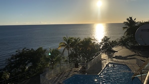 A pool area with a view of the ocean and a sunset.