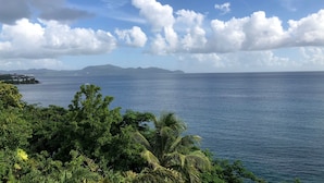 A coastal landscape with a view of the sea, distant mountains, and lush greenery.