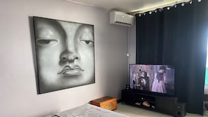 A bedroom with a bed, a television, a wall-mounted air conditioner, and a window with curtains.