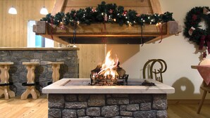 A stone fireplace with a fire burning, wooden beams above, and Christmas decorations. - Alpine Aria (Kalavrita)