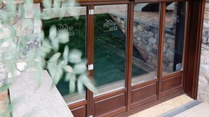 A stone exterior wall with a wooden overhang and a glass door with the name 'Alpine Aria' written on it. - Alpine Aria (Kalavrita)