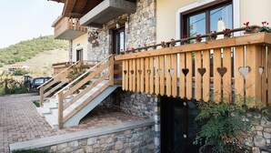 A stone building with a wooden staircase leading to a balcony with heart-shaped cutouts. - Alpine Aria (Kalavrita)