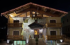A two-story building with a stone facade, wooden balconies, and a lit entrance. - Alpine Aria (Kalavrita)