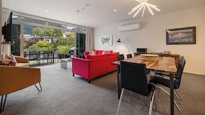 Ein modernes Wohnzimmer mit einem roten Sofa, einem Esstisch mit Stühlen und einem großen Fenster mit Blick auf einen Balkon und Gartenmöbel.