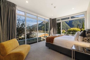A modern bedroom with a large bed, a sofa, and a view of mountains through floor-to-ceiling windows. - Edgar Rise, 500m from Queenstown CBD (Queenstown Hill)