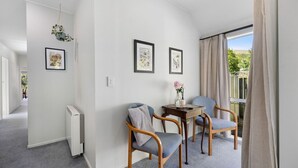 Une chambre moderne avec une grande fenêtre, deux fauteuils, une petite table et des œuvres d’art encadrées accrochées aux murs.