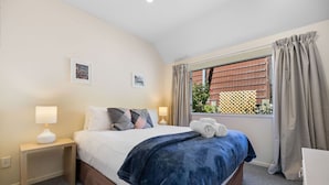 Une chambre à coucher bien rangée, avec un lit, deux tables de chevet, une fenêtre avec des rideaux et une vue sur l’extérieur.