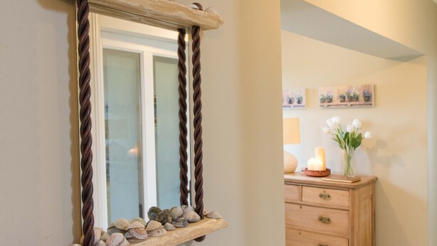 Un miroir avec un cadre rustique, une étagère en bois ornée de coquillages et une commode sur laquelle est posé un vase de fleurs.