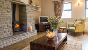 Un salon chaleureux avec une cheminée en pierre, un téléviseur, un fauteuil confortable et un vase rempli de fleurs posé sur une table basse en bois.