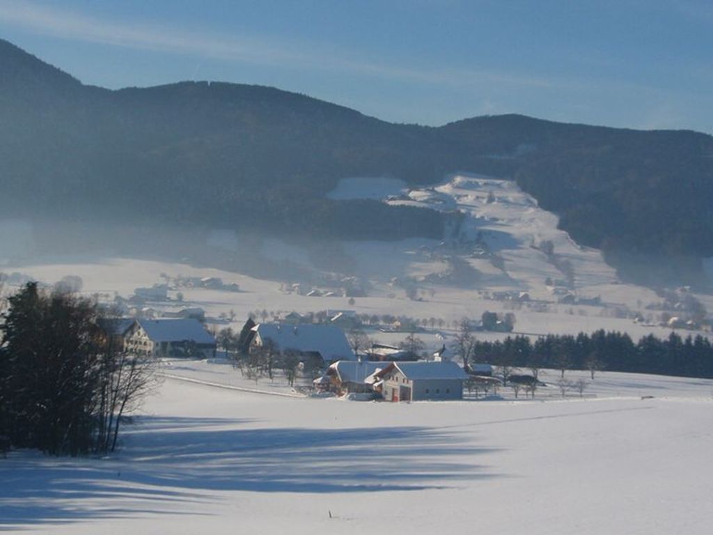 Een besneeuwd landschap met enkele gebouwen, waaronder een huis met een rode deur en een schuur, omringd door bergen.