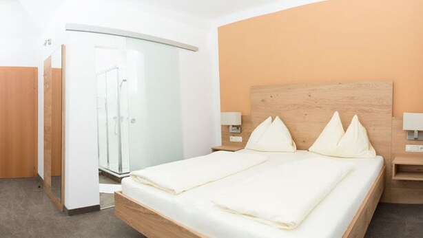 Een moderne hotelkamer met een houten bed, een douchecabine van glas en een gebogen plafond.