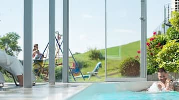 Ein Hallenbad mit großen Glaswänden, einer Rutsche und Blick auf eine grüne Landschaft.