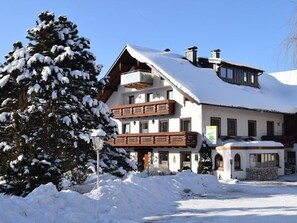 A snow-covered building with a balcony and a snow-covered tree in front.