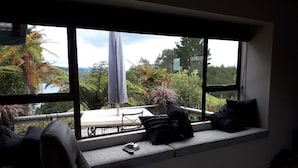 Une pièce dotée d’une grande fenêtre donnant sur un jardin et un plan d’eau. On aperçoit un canapé et un fauteuil au premier plan.