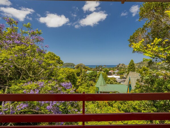 A lush green landscape with a view of the ocean and a building with a green roof. - Treetop Bach - Hahei Bach (Hahei)