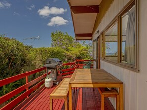 A wooden deck with a barbecue grill, a table, and chairs. - Treetop Bach - Hahei Bach (Hahei)