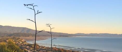 A coastal town with houses along the beach, a clear sky, and mountains in the background.