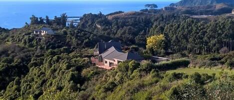 A house surrounded by dense forest and hills with a view of the sea.