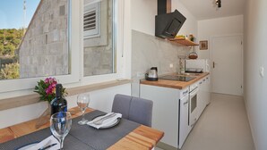 Une cuisine de taille réduite avec une façade en pierre, un coin repas avec une table dressée pour deux personnes, et une vue sur l’extérieur.