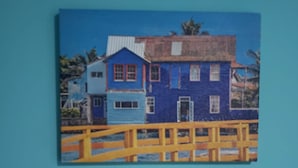 A painting of a two-story house with a blue facade and a yellow fence in front. - Plaza del Mar (San Andrés)
