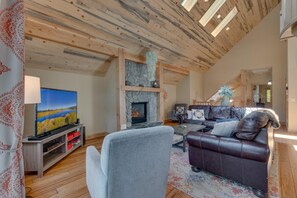 Ein Wohnzimmer mit Kamin, Fernseher, Ledermöbeln und einer Holzbalkendecke.