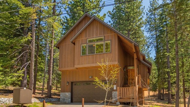 Une cabane en bois à deux étages, dotée d’un garage, entourée d’arbres.