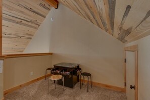 Ein Zimmer mit schrägem Dach, einem Tischfußballtisch, zwei Hockern und einer Tür.