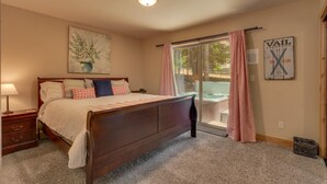 Une chambre à coucher avec un lit, des tables de chevet, une lampe, un tableau, une porte-fenêtre coulissante et un panneau sur le mur.