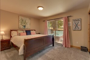 Una camera da letto con un letto, comodini, una lampada, un quadro, una porta finestra e un cartello appeso al muro.