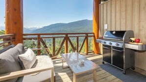 Eine Holzterrasse mit Grill und Sitzgelegenheit mit Blick auf eine gebirgige Landschaft.