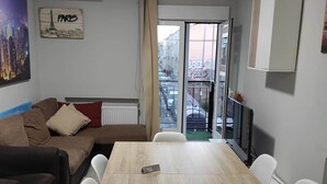 A modern living room with a sofa, a dining table, and a view of the street through a glass door. - Barajas Apartment. Airport/IFEMA (Madrid)