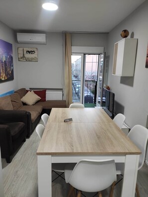 Una sala de estar moderna con un sofá, una mesa de comedor y vista a la calle a través de una puerta de vidrio.