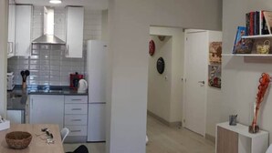 A modern kitchen with white cabinets, a stainless steel range hood, and a dining area with a table and chairs. - Barajas Apartment. Airport/IFEMA (Madrid)