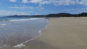 Ein weiter Sandstrand mit sanften Wellen, blauem Himmel und Hügeln in der Ferne.