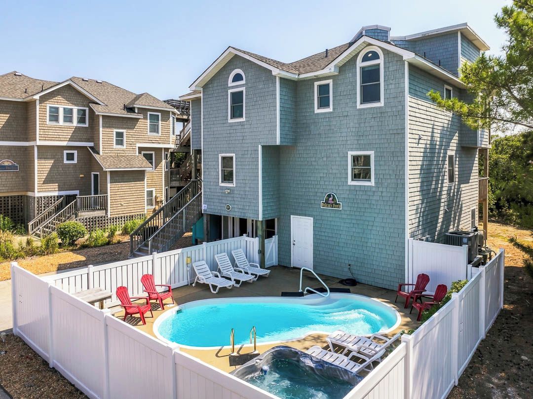 A residential building with a backyard pool and hot tub, surrounded by a white fence.
