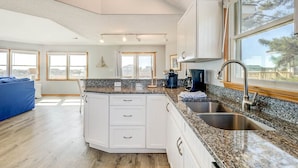 A modern kitchen with white cabinetry, granite countertops, and a large window offering a view of the outdoors. - Pelican's Perch | 320 ft from the beach | Private Pool, Hot Tub | Corolla (Corolla)