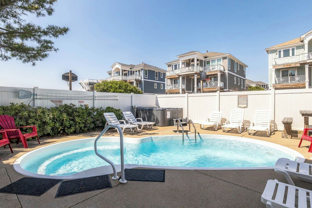 A swimming pool with lounge chairs and a hot tub, surrounded by buildings with balconies.