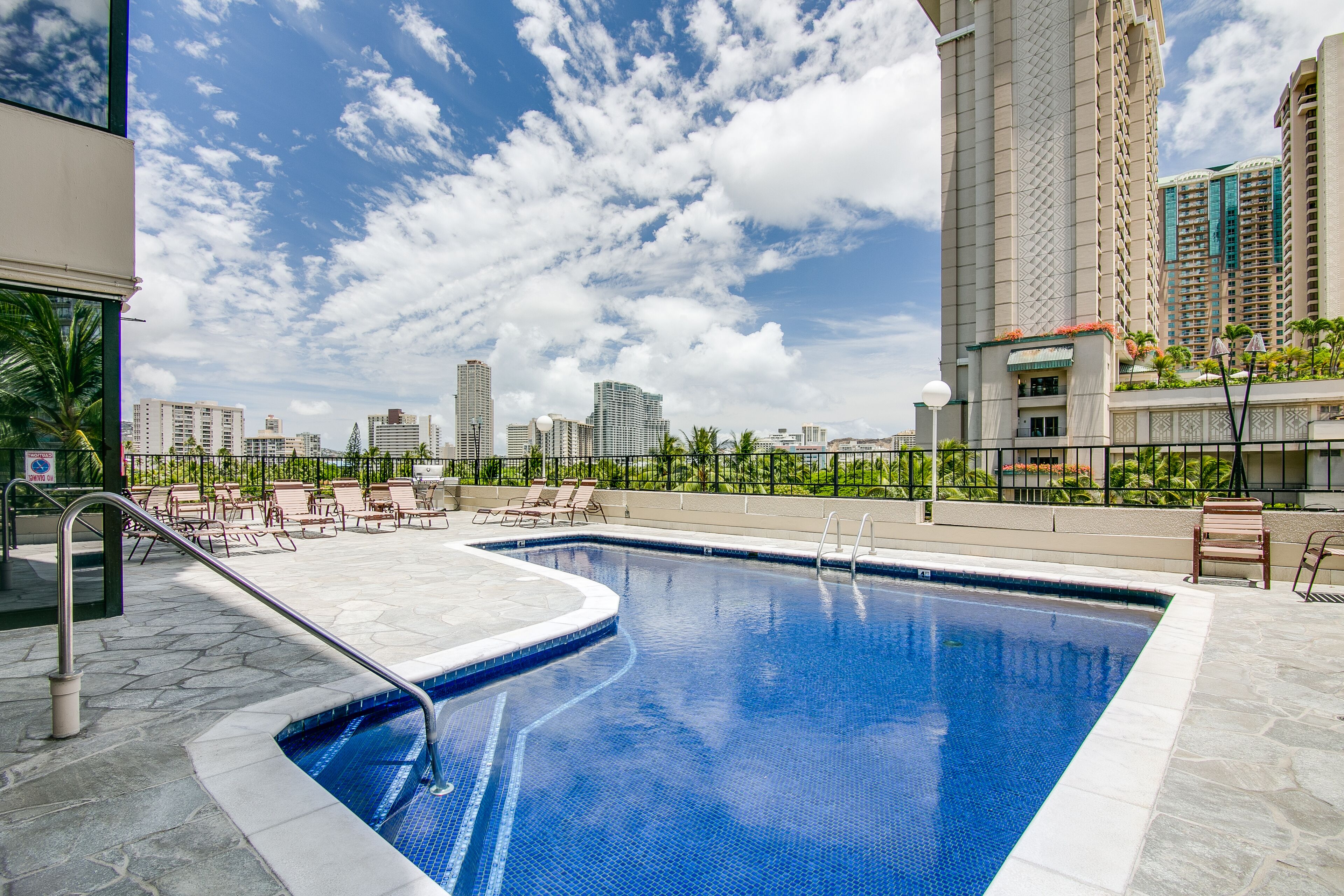 Una piscina en la azotea con vistas despejadas al horizonte de la ciudad, rodeada de sillones de descanso y una terraza de piedra.