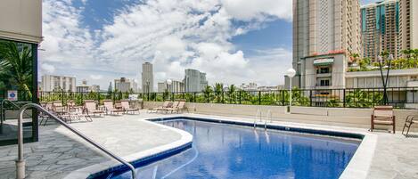 Una piscina en la azotea con vistas despejadas al horizonte de la ciudad, rodeada de sillones de descanso y una terraza de piedra.