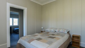 A bedroom with a large bed, a nightstand, a wooden shelf, and a window with daylight coming through.