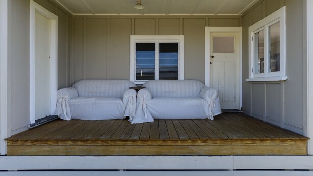 A covered porch with a wooden deck, two white upholstered sofas, and a small table.