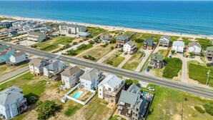 Vue aérienne d’une zone résidentielle côtière, avec des maisons, une route et une plage.