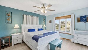 Une chambre à coucher comprenant un lit, des tables de chevet, un banc, un ventilateur de plafond et une fenêtre avec des rideaux.