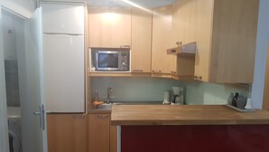 Una cocina compacta con microondas, cafetera y un lavamanos pequeño.
