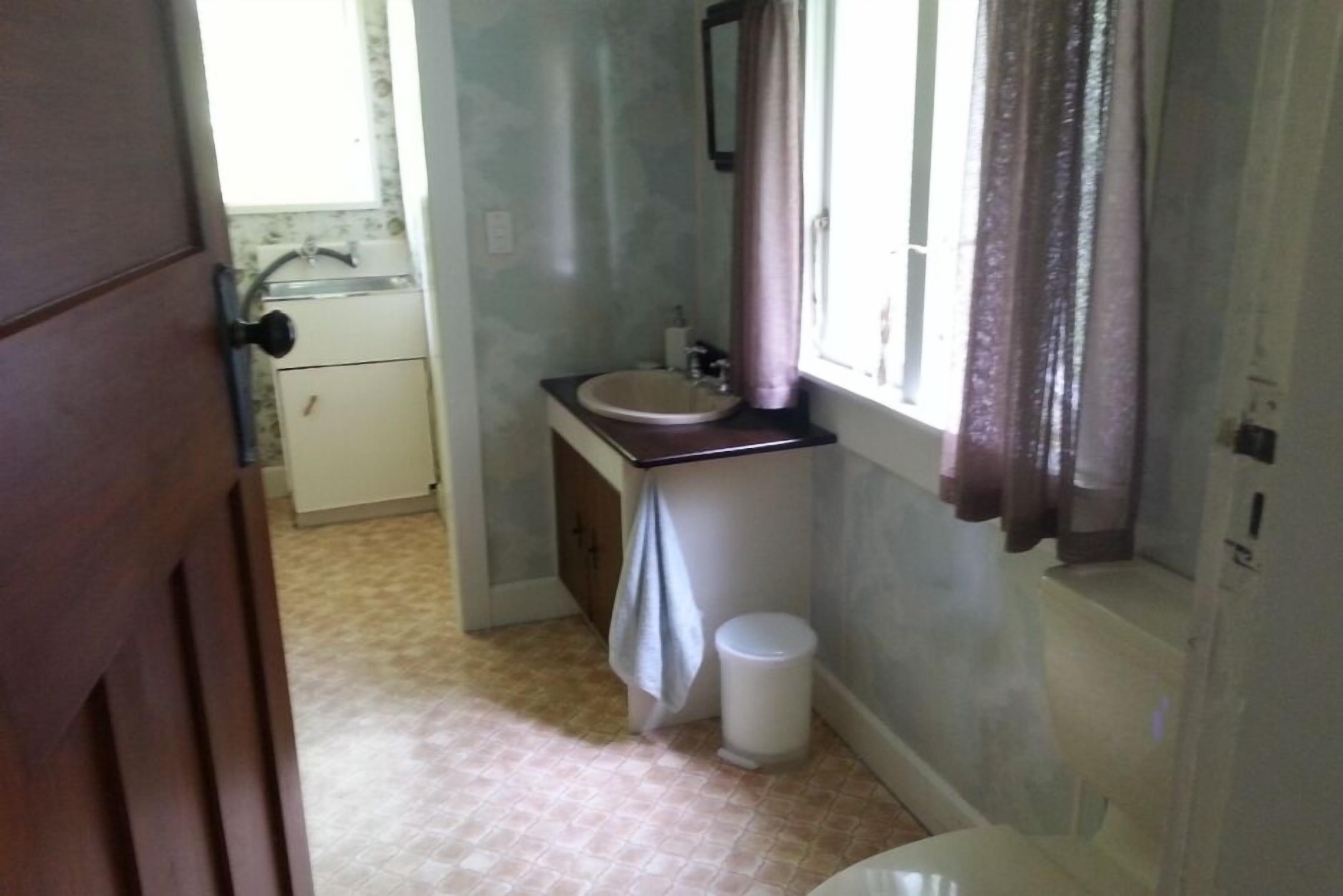 Un baño con lavamanos, inodoro y ventana con cortinas.