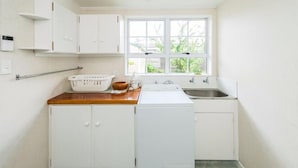A compact kitchen with white cabinets, a wooden countertop, a washing machine, a sink, and a window with a view of greenery. - Charmae Guest House by the river.
7 x Beds, (sleeps 10)
Plus powered van site (Wanganui Township)