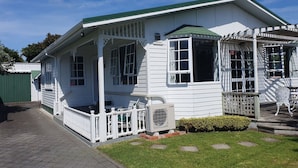 A white house with a green roof, a porch with a white railing, and a small garden area. - Charmae Guest House by the river.
7 x Beds, (sleeps 10)
Plus powered van site (Wanganui Township)
