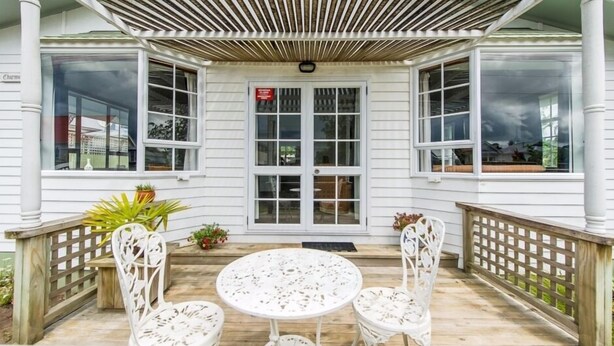 A covered patio with a white table and chairs, a wooden fence, and a door with a sign. - Charmae Guest House by the river.
7 x Beds, (sleeps 10)
Plus powered van site (Wanganui Township)